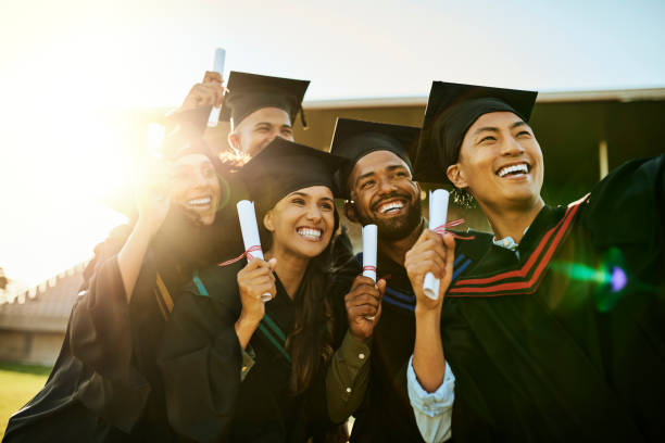 Diverse group of happy graduates in gowns taking a selfie with phone at graduation. Cheerful motivated qualified students capturing memorable photos and celebrating academic achievement and milestone